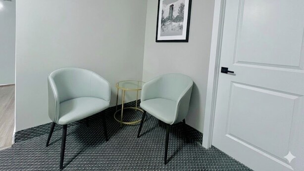 Una habitación con dos sillas de colores claros, una mesita redonda, un cuadro en la pared y una puerta blanca.