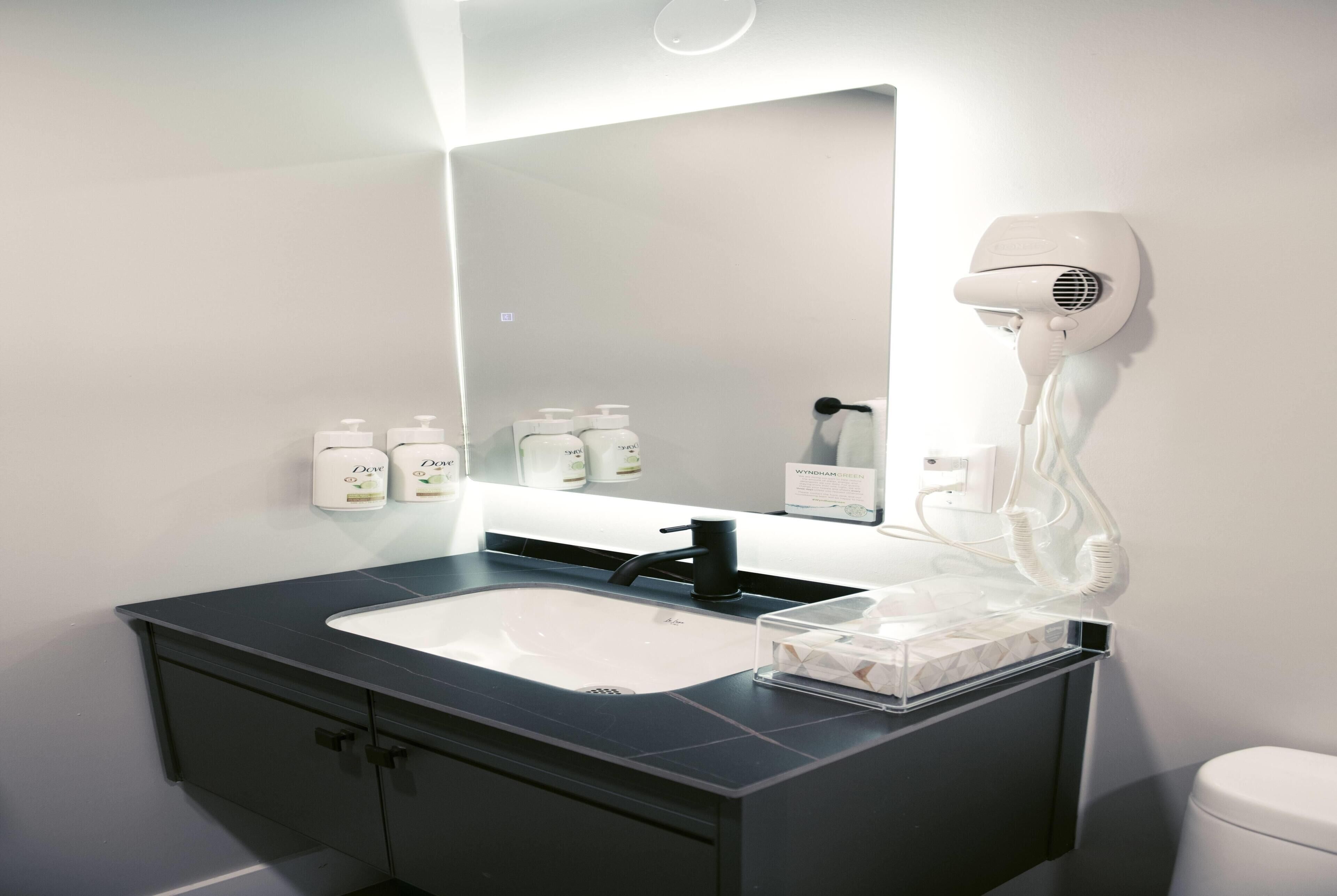 A modern bathroom with a white sink, dark countertop, and a hairdryer mounted on the wall.