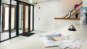 Un área de recepción con puerta de entrada de vidrio, mostrador de recepción, timbre y folletos informativos.