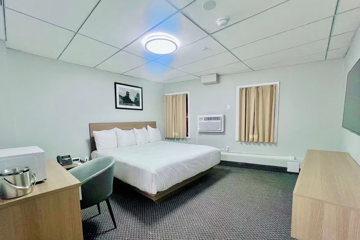 Habitación de hotel con cama, escritorio con teléfono, una silla, microondas, aire acondicionado y un cuadro en la pared.