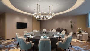 Une salle de conférence équipée d’une table ronde, de chaises, d’un lustre, d’un téléviseur à écran plat et d’une plante décorative.