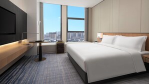 Une chambre d’hôtel moderne dotée d’un grand lit, d’un téléviseur à écran plat, d’une petite table et offrant une vue sur le paysage urbain grâce à de grandes fenêtres.