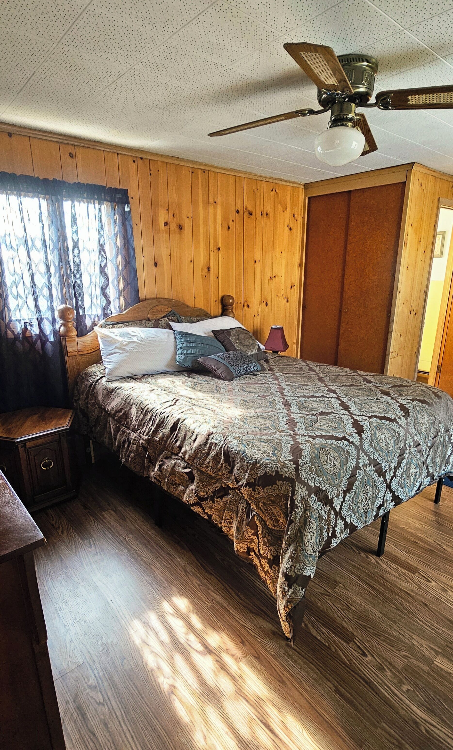 A bedroom with a wooden bed, a nightstand, a lamp, and a ceiling fan.
