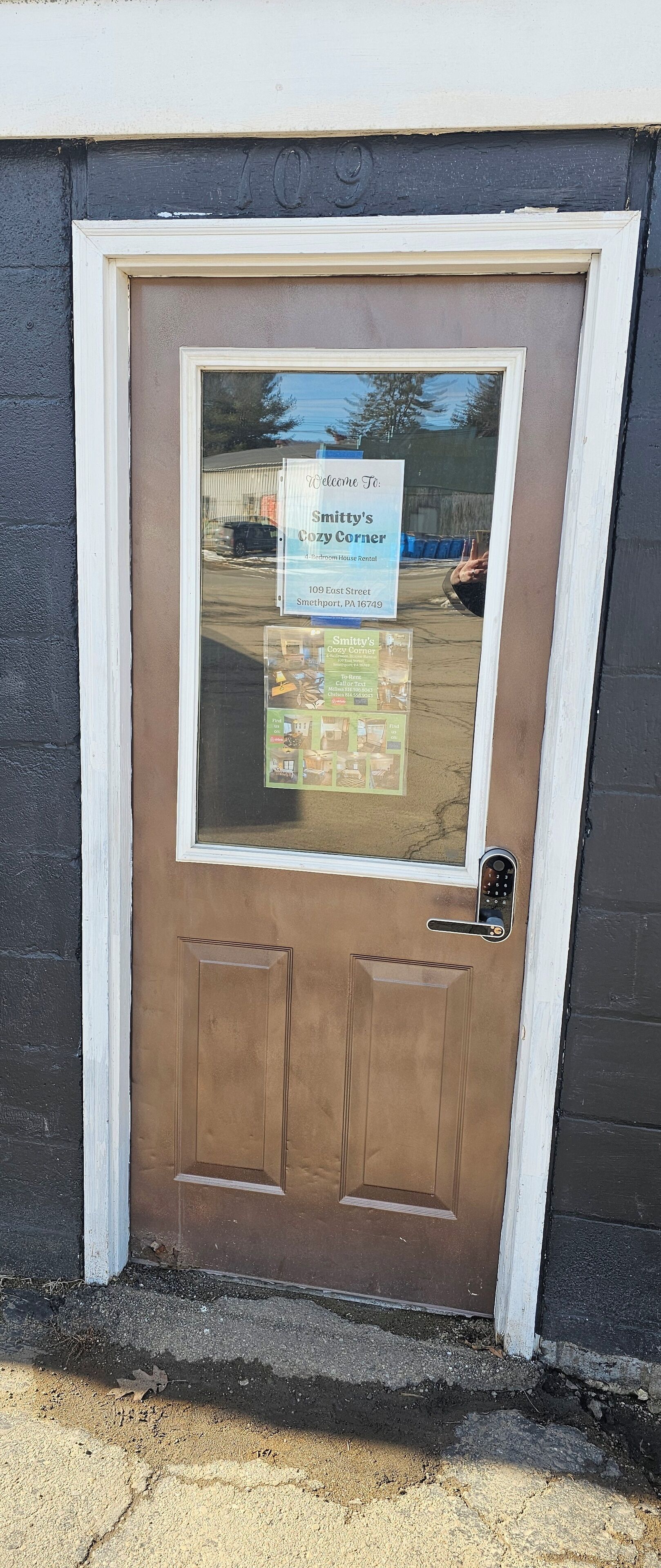 A brown door with a window, a sign reading "Welcome To Smitty's Cozy Corner," and a keypad lock.