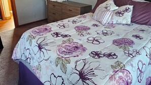 A bedroom with a floral bedspread, a dresser, a mirror, and a painting on the wall. - Smitty's Cozy Corner in Smethport, PA. Spaciously 4-bedroom home (Smethport)