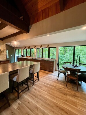 A modern kitchen with a large island, wooden flooring, and large windows offering a view of greenery. - Massanutten, Parkway, JMU and Vineyards Galore- sleeps 12 (Elkton)