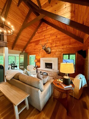 A log cabin interior with a fireplace, a mounted deer head, a sofa, and a dining table. - Massanutten, Parkway, JMU and Vineyards Galore- sleeps 12 (Elkton)