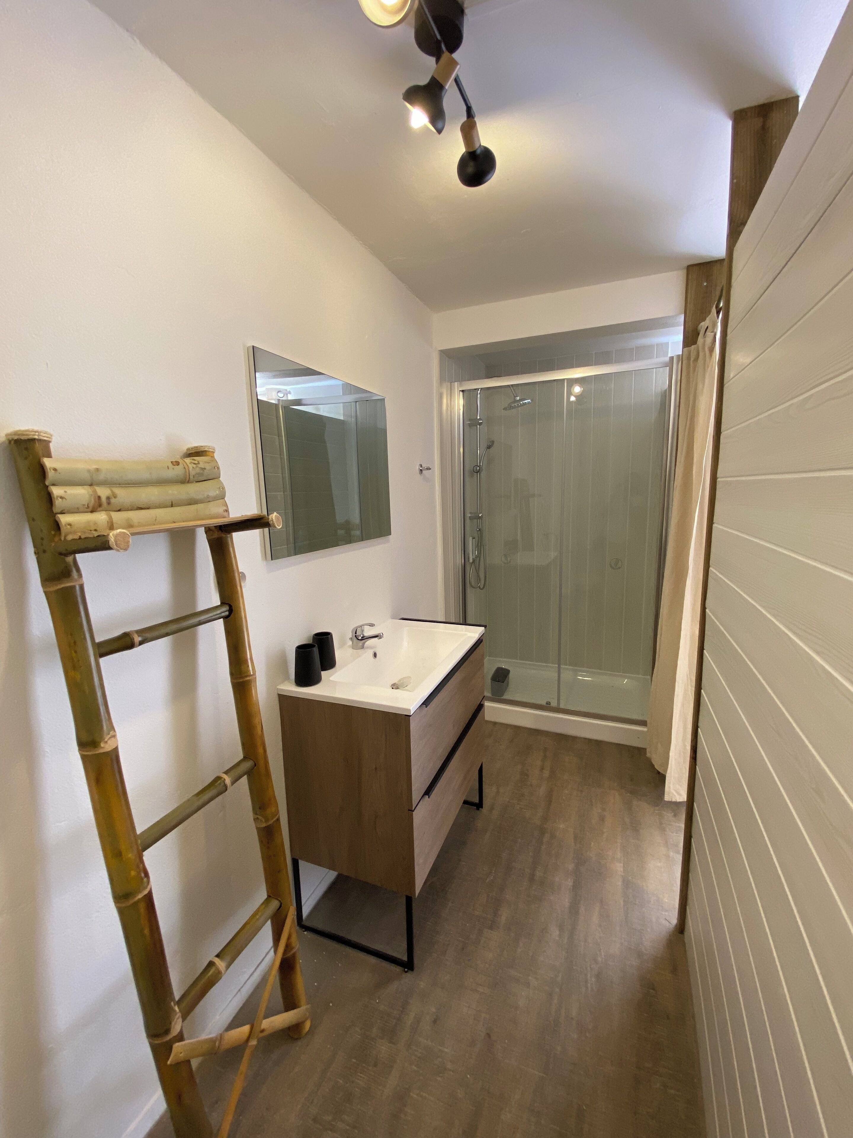 A bathroom with a wooden ladder, a sink, a mirror, and a shower.