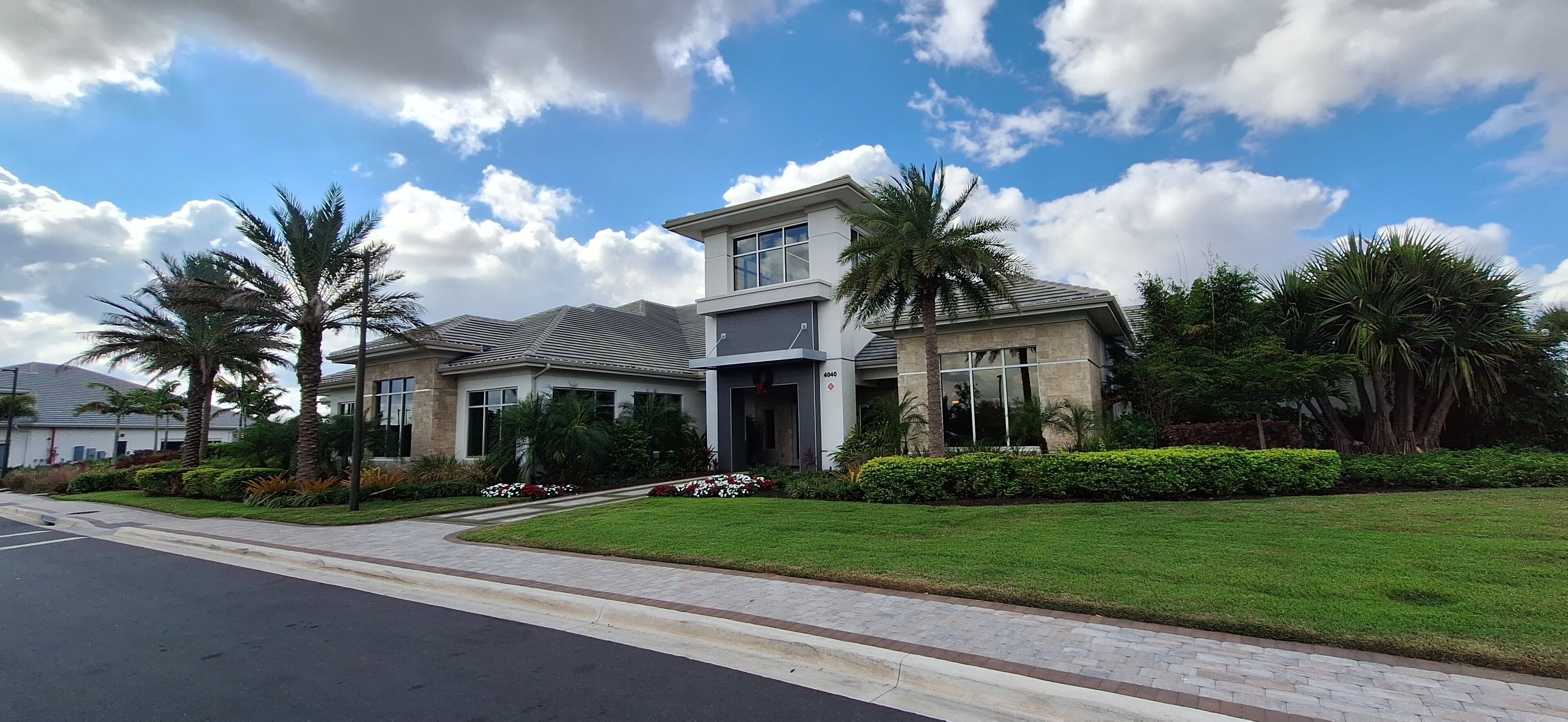 A modern two-story house with a well-maintained lawn, palm trees, and a clear blue sky.