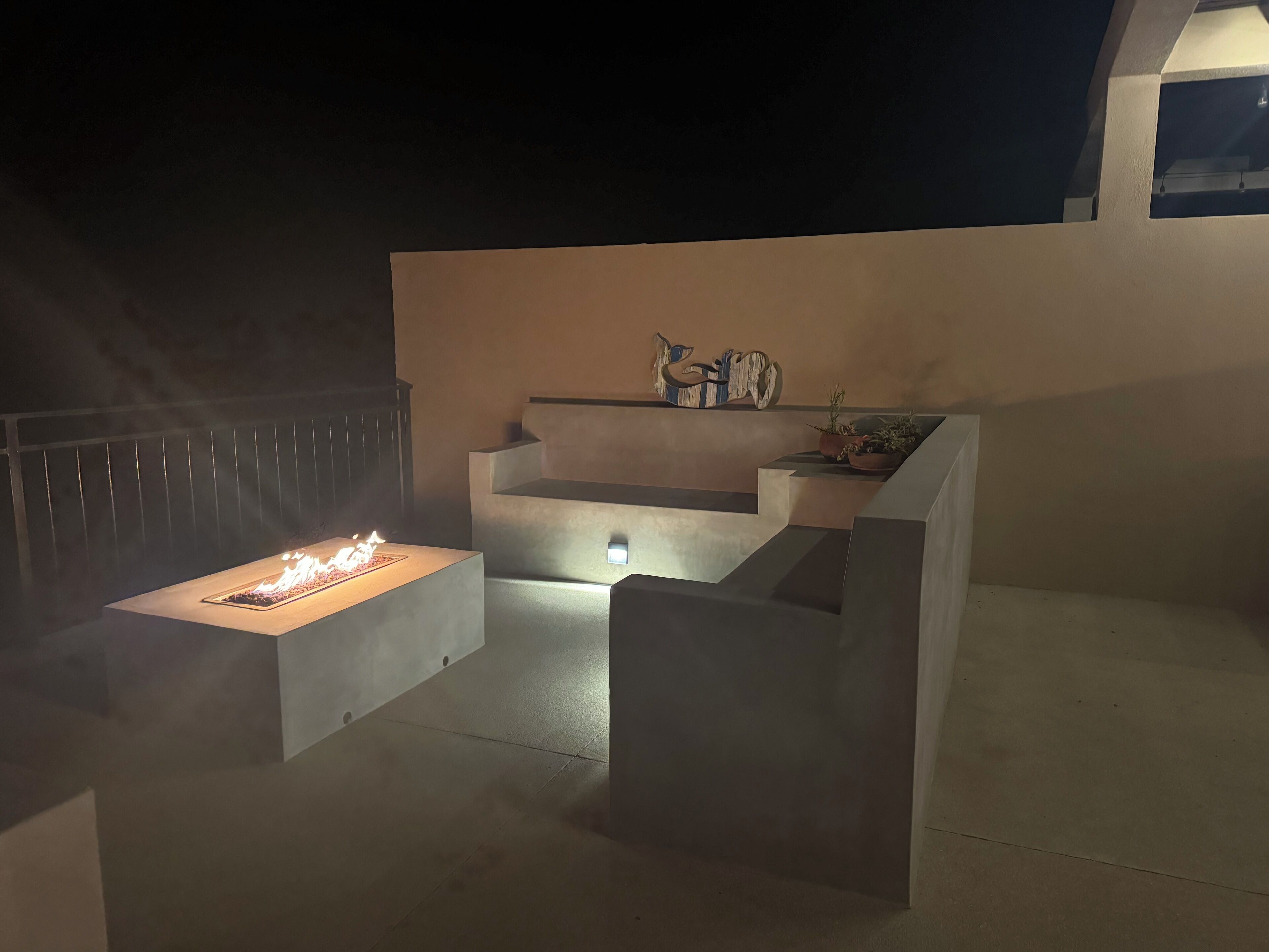 A modern outdoor patio with a central fire feature, a built-in bench, and a small table with potted plants.