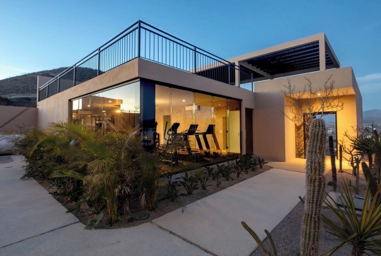 A modern house with a balcony, a patio with exercise equipment, and a cactus garden.