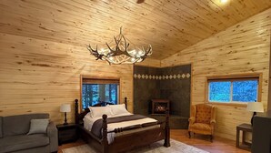 Um quarto de cabana de madeira aconchegante, com teto de madeira, uma cama grande, lareira e um lustre.