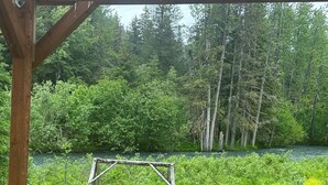 Um deck de madeira com um banco, de frente para um rio, rodeado por floresta densa e vegetação.