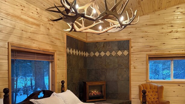Quarto de cabana rústica com uma cama grande, lareira e um candelabro de galhos de veado.