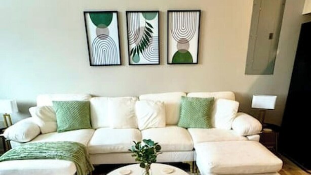 A living room with a white sofa, green cushions, a round coffee table with a plant, and abstract wall art. - Chic Serenity Loft / Fast Wi-Fi Walkable (Cleveland)