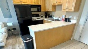 A compact kitchen with wooden cabinets, a black refrigerator, a microwave, and a small island counter. - Chic Serenity Loft / Fast Wi-Fi Walkable (Cleveland)