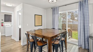 A dining area with a wooden table and chairs, a ceiling light, and a view of the backyard through a sliding glass door.