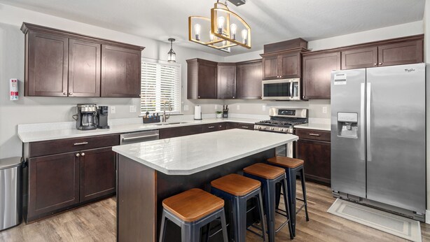 A modern kitchen with dark wood cabinets, a large island with stools, stainless steel appliances, and a pendant light.