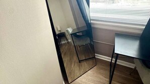 A room with a large mirror, a small table, and a chair. There is a power outlet on the wall.
