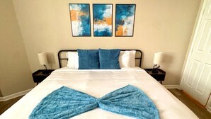 A hotel room with a bed, two bedside tables, and three abstract paintings on the wall.