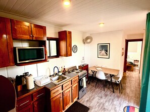 A compact kitchen with wooden cabinets, a microwave, a sink, and a dining area with a table and chairs. - Las Ballenas de Avellanas (Playa Avellanas)