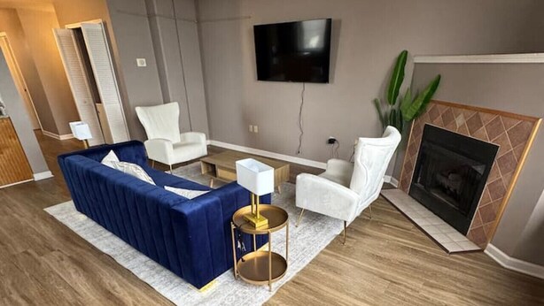 Un salon moderne avec un canapé d’angle bleu, des fauteuils blancs, une petite table d’appoint ronde dorée et un téléviseur à écran plat fixé au mur.