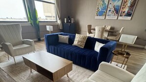 Un salon moderne avec un canapé bleu, des fauteuils blancs et une table basse en bois.