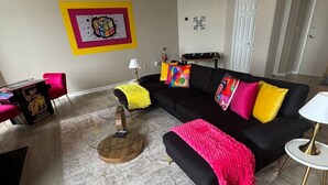 Uma sala de estar moderna com um sofá preto, almofadas coloridas, uma mesa de centro de madeira e um tapete de mármore.