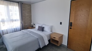 Ein Schlafzimmer mit einem Bett, Nachttischen, einer Holztür und einem Fenster mit Vorhängen.