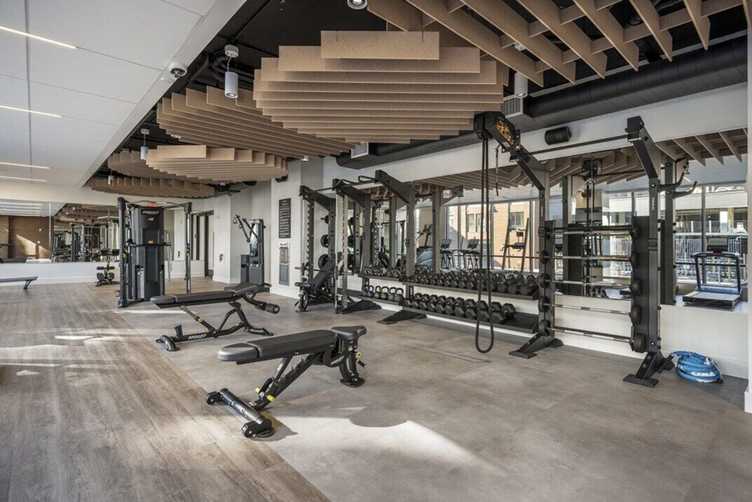 A modern gym with various exercise equipment, a bench, and a mirrored wall.