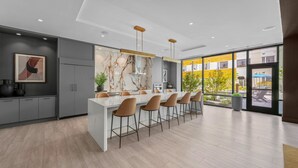 A modern kitchen with a marble backsplash, a central island with bar stools, and large windows offering a view of the outdoors. - Hyatus Curated Residences Everett (Everett)