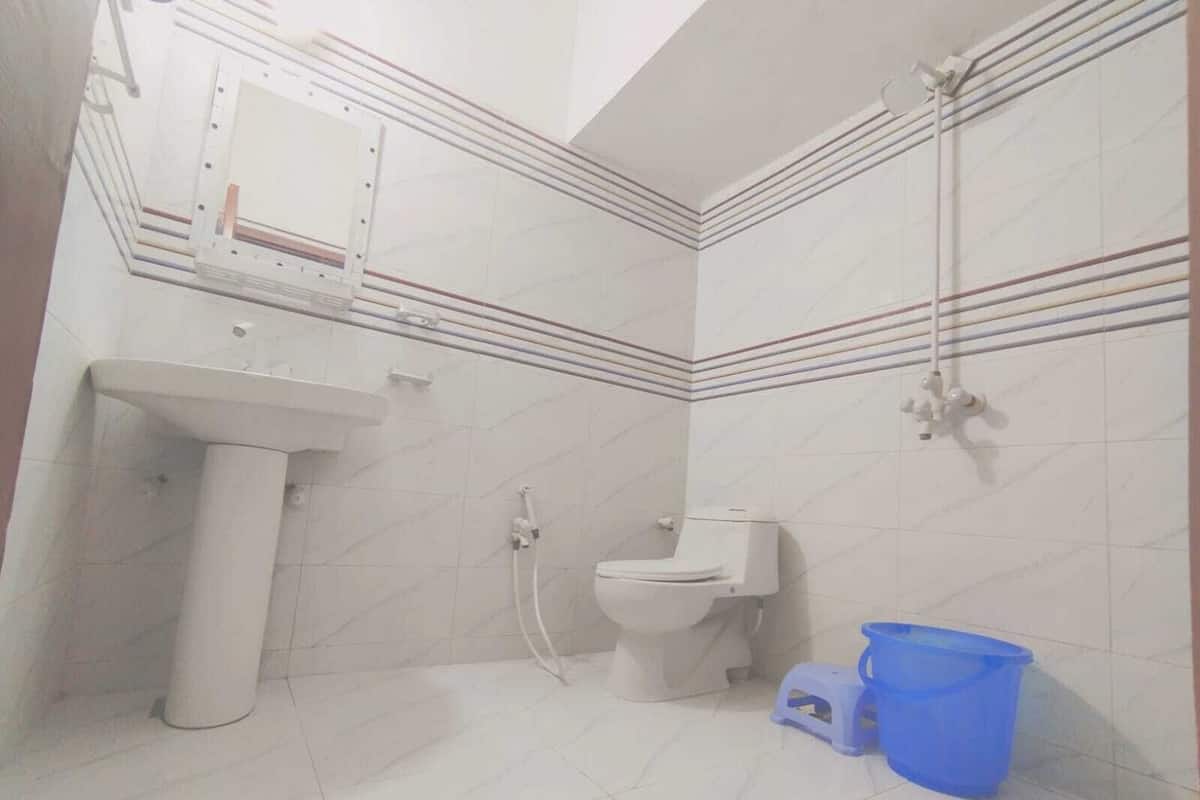Een badkamer met een wastafel op voetstuk, toilet, douche en een blauwe plastic bak.