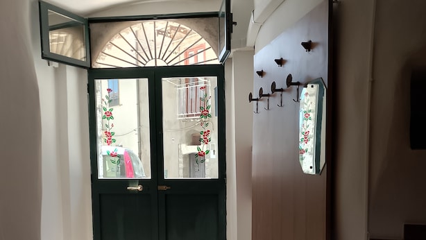A hallway with a green door, a fan, and a television displaying a news program. - Studio apartment in the historic center renovated (Pietragalla)