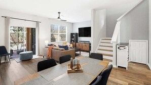 Een moderne woonruimte met een eethoek, bank, televisie, trap en een schuifdeur naar een buitenruimte.