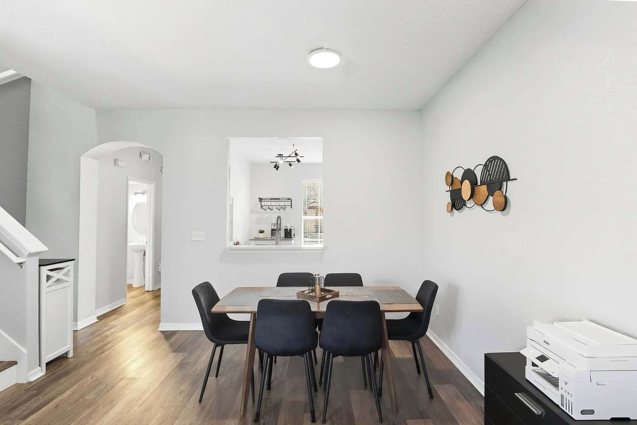 A modern dining area with a rectangular table, black chairs, and a white printer on a black stand.