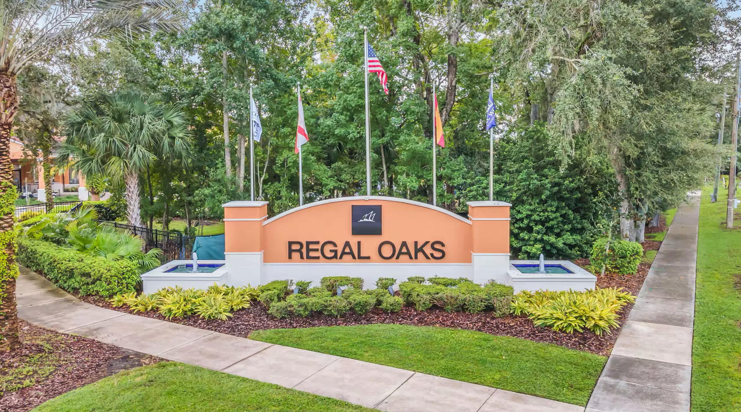 A sign for Regal Oaks with a landscaped entrance and multiple flags.