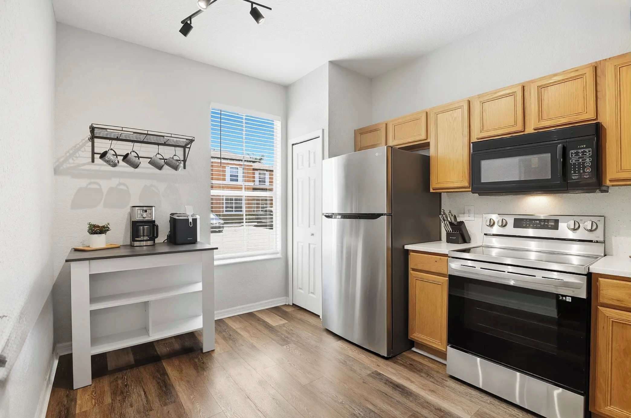 A modern kitchen with stainless steel appliances, wooden cabinets, and a window with blinds.