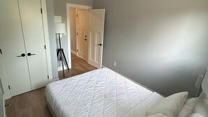 Une chambre à coucher comprenant un lit, une table de chevet, une lampe et une porte donnant sur une autre pièce.