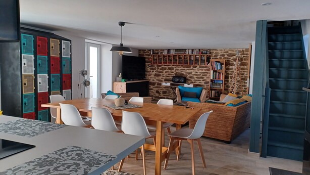 Un comedor con una mesa de madera y sillas blancas, una estantería de pared de piedra y una escalera azul.
