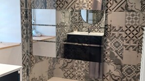 Baño con azulejos estampados, un espejo, un lavabo y una zona de ducha.