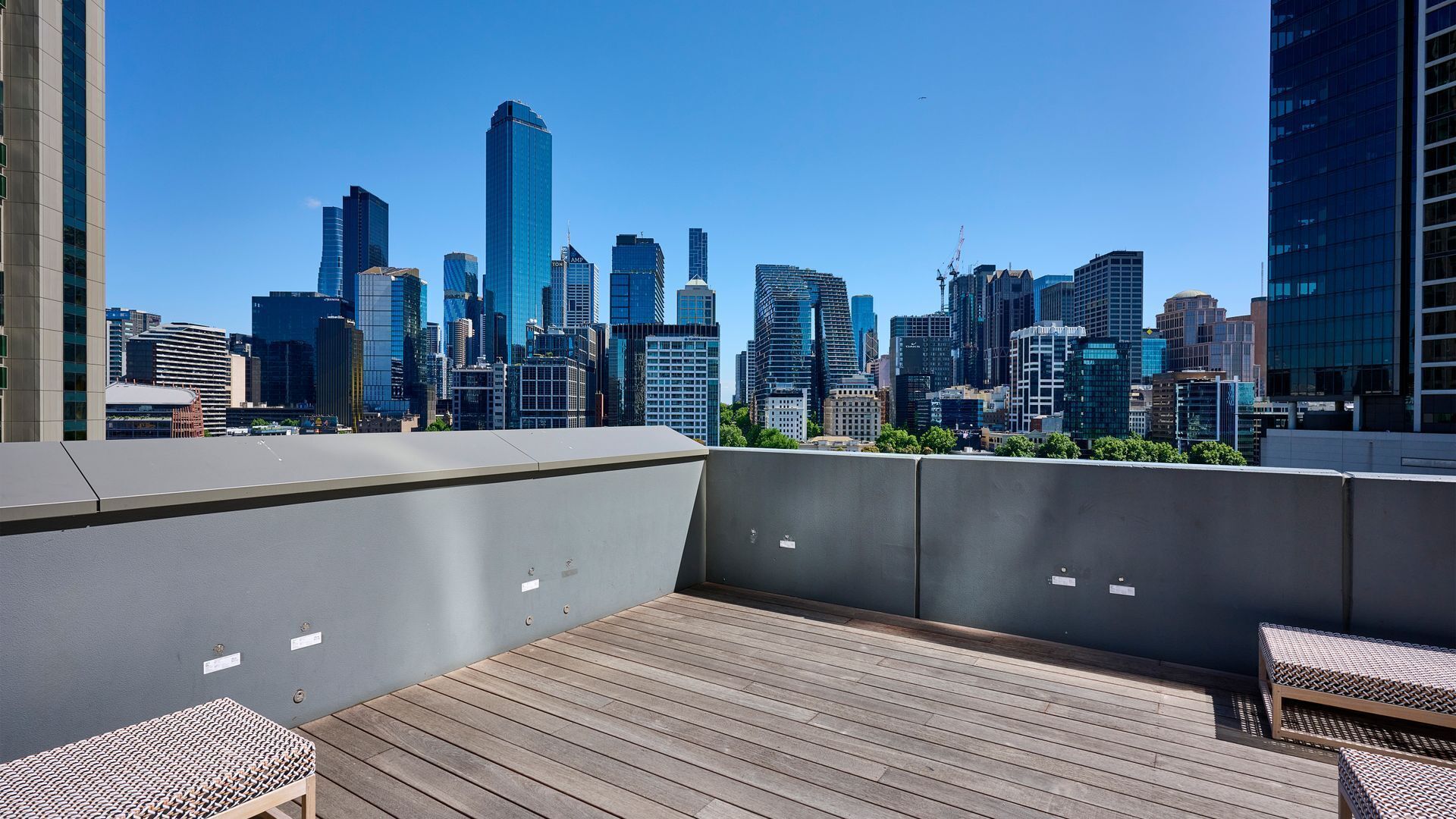 A rooftop terrace with a city skyline view, wooden flooring, and outdoor seating.
