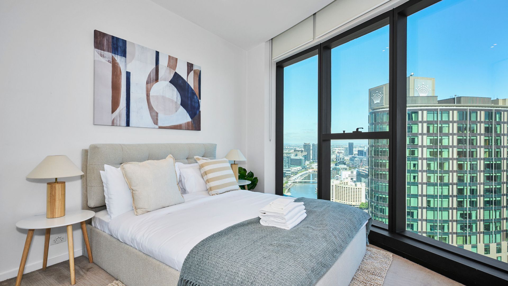 Ein modernes Schlafzimmer mit einem großen Bett, Blick auf eine Stadtlandschaft und einem Bild an der Wand.