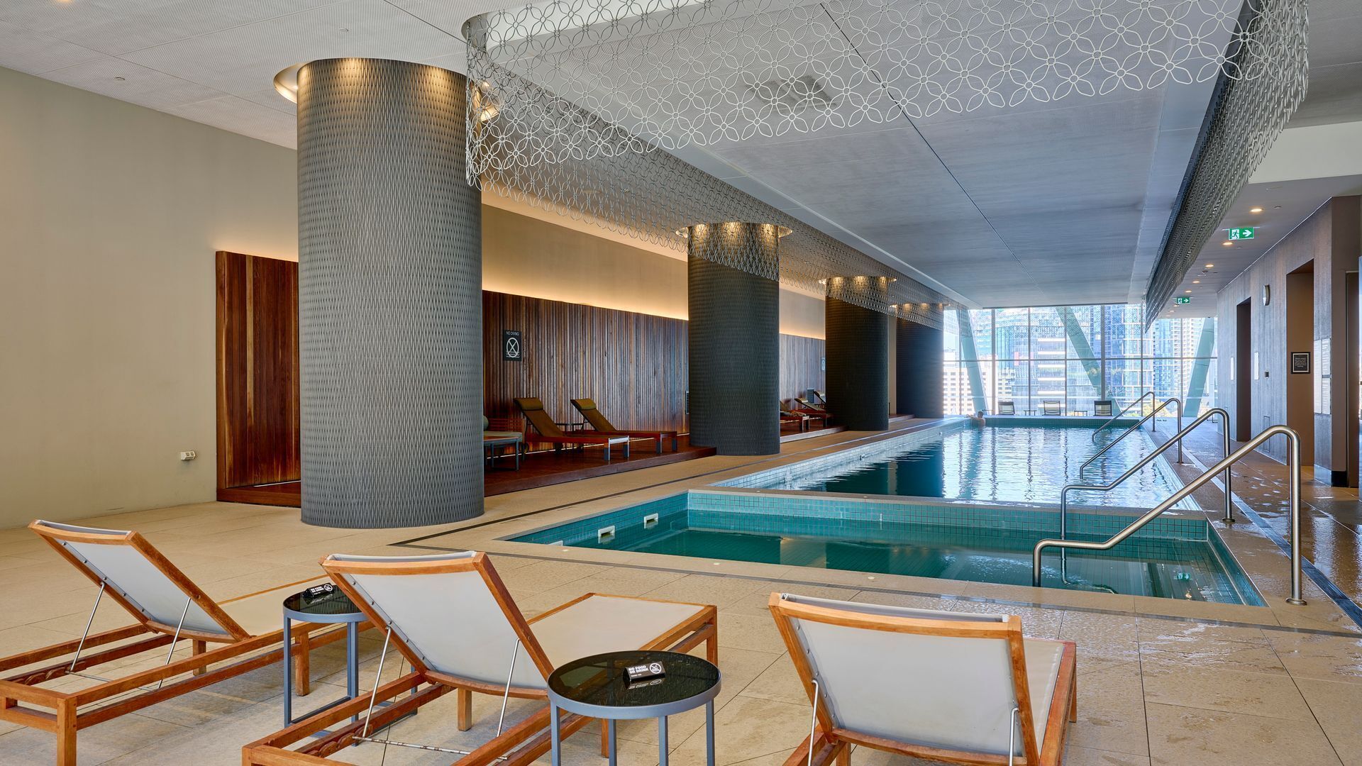 Una piscina interna moderna con sedie a sdraio e un soffitto alto decorato con motivi geometrici.