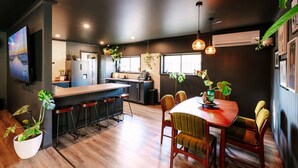 Una cocina moderna con una isla central, taburetes de bar y una zona de comedor con mesa y sillas de madera.