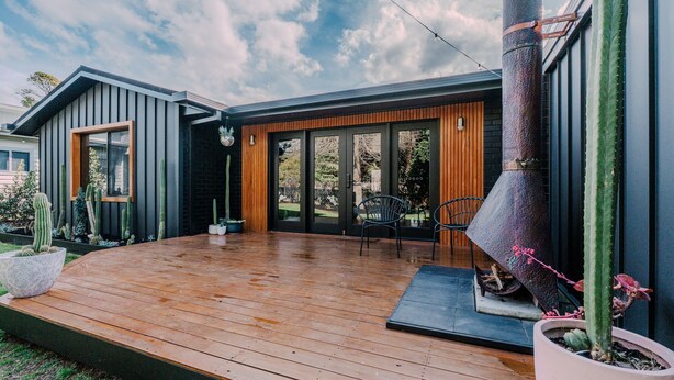 Una casa moderna con terraza de madera, una chimenea grande y un jardín con cactus.