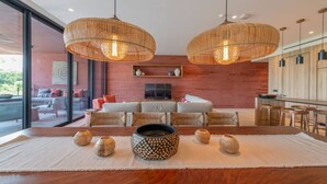 Uma sala de estar moderna com uma grande mesa de jantar de madeira, duas luminárias de vime suspensas e uma parede de tijolos vermelhos.