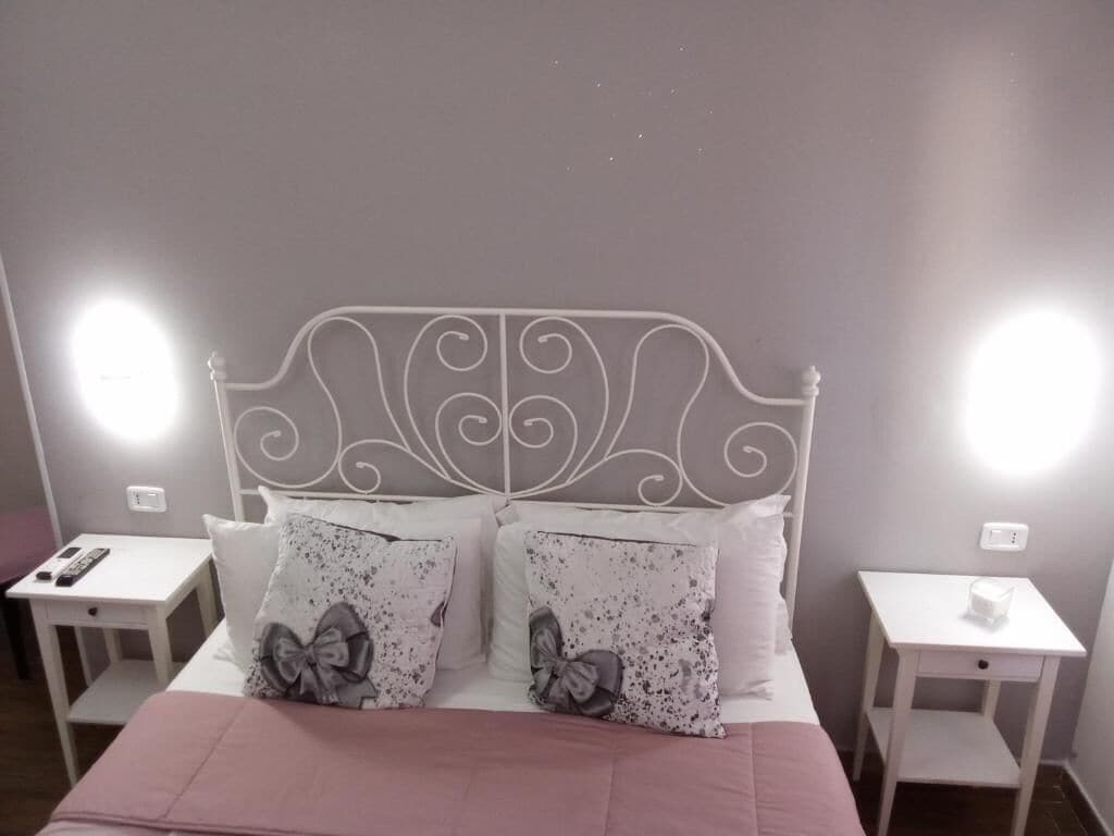 Ein ordentlich eingerichtetes Schlafzimmer mit einem Metall-Kopfteil, zwei Nachttischen und einem Bett mit einer rosa Tagesdecke und gemusterten Kissen.