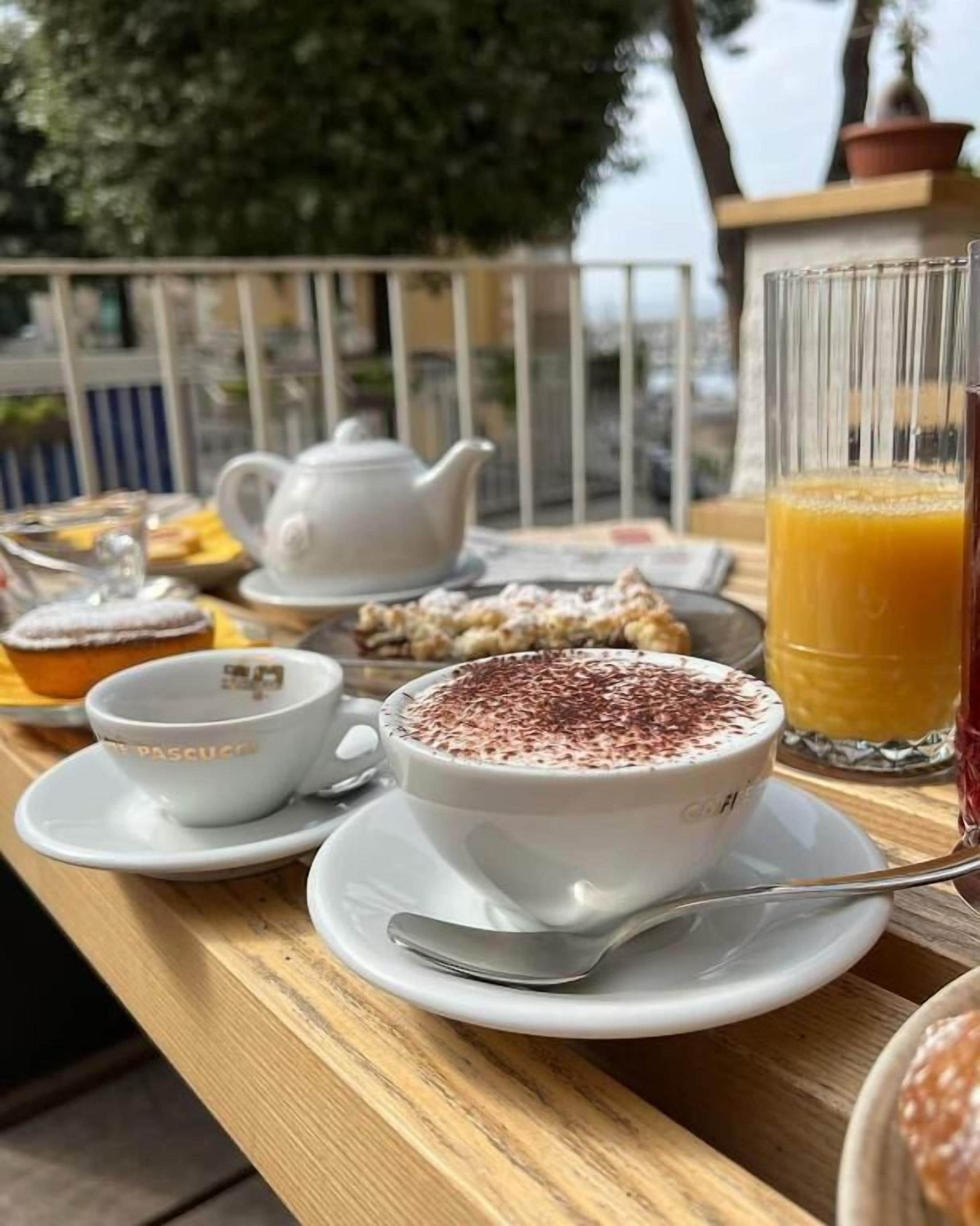 A table set with a teapot, cups, a glass of orange juice, and pastries.