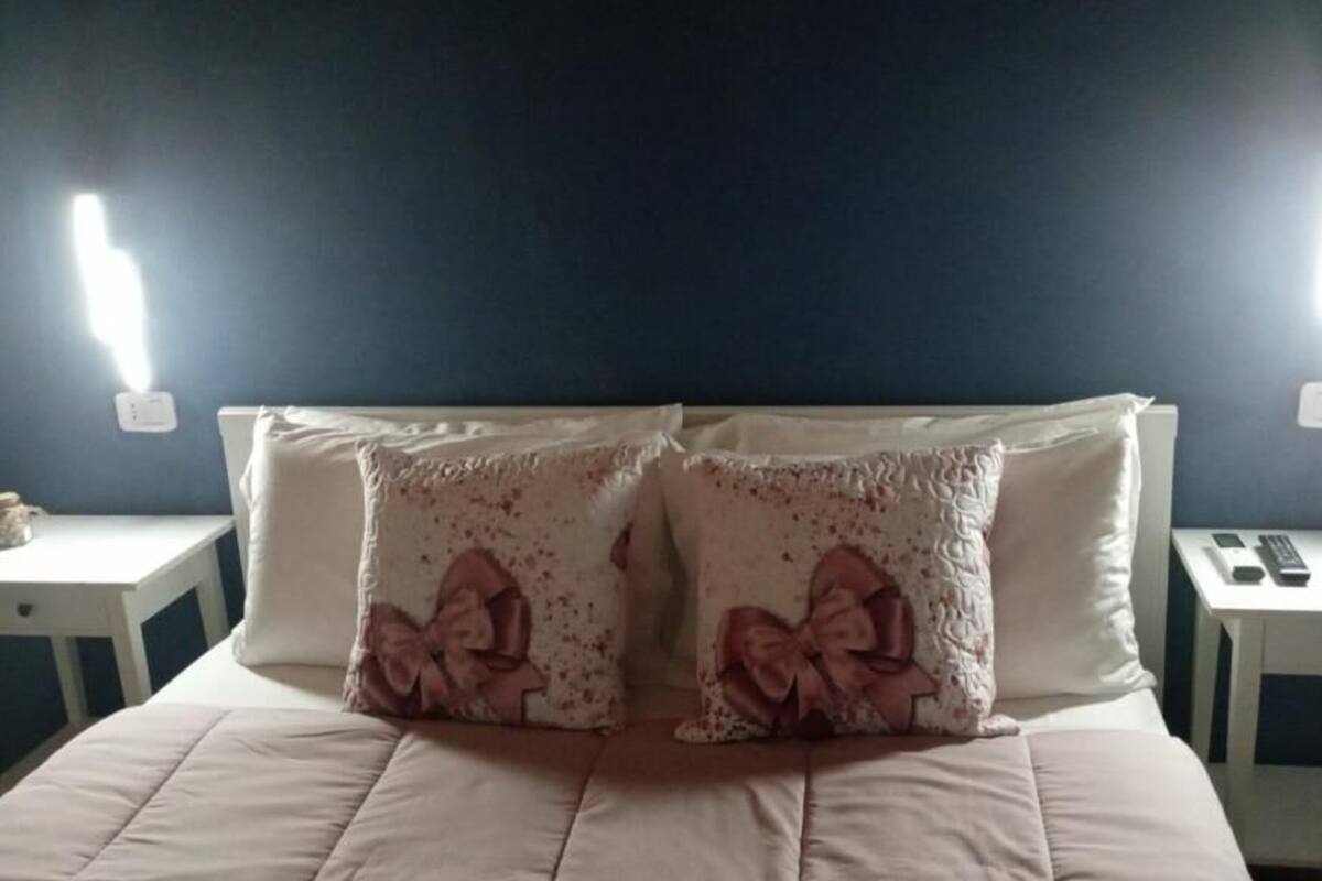 Un lit avec deux oreillers, une table de chevet et un luminaire fixé au mur.