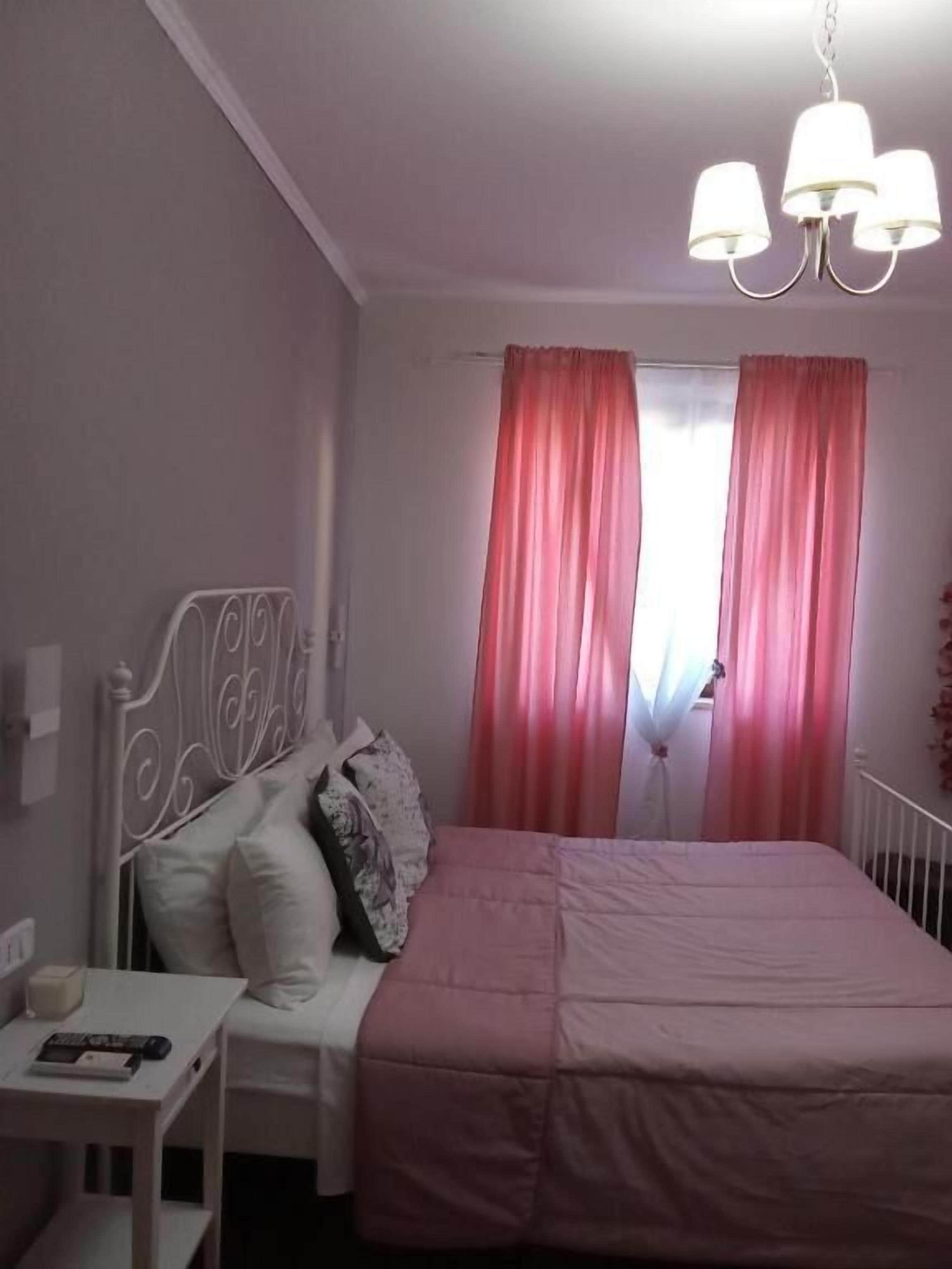 Un dormitorio con cama, mesita de noche, lámpara y ventana con cortinas.